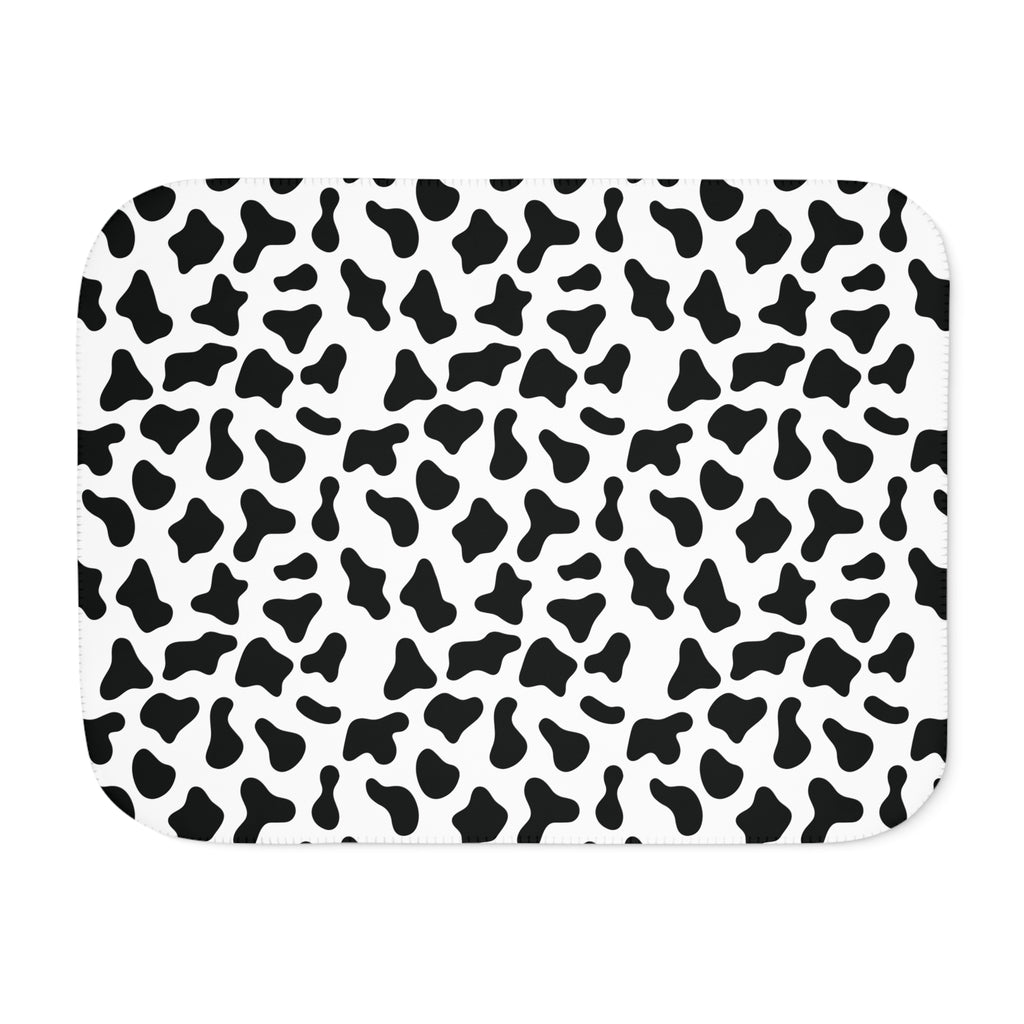 Black and white cow print sherpa blanket laid flat, showing irregular black patches on white with a white sherpa edge
