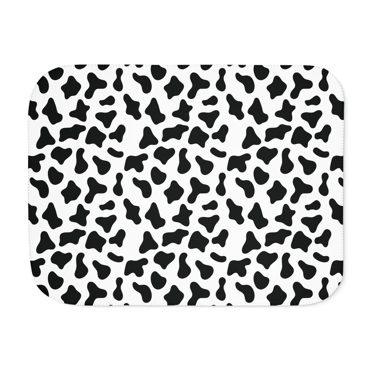 Black and white cow print sherpa blanket laid flat, showing irregular black patches on white with a white sherpa edge