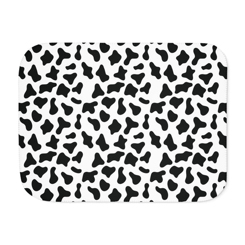 Black and white cow print sherpa blanket laid flat, showing irregular black patches on white with a white sherpa edge