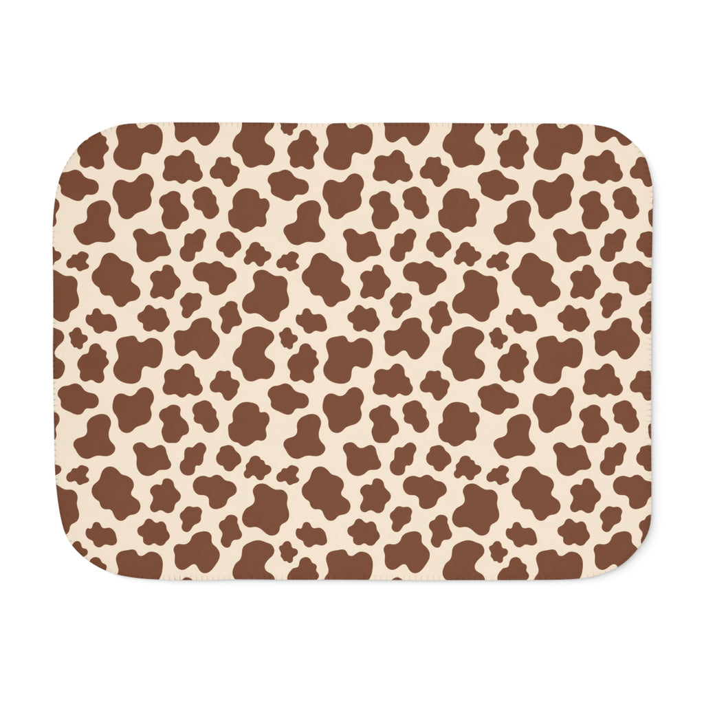Brown cow print sherpa blanket laid flat, showing chocolate brown patches on a cream ground with a white sherpa edge
