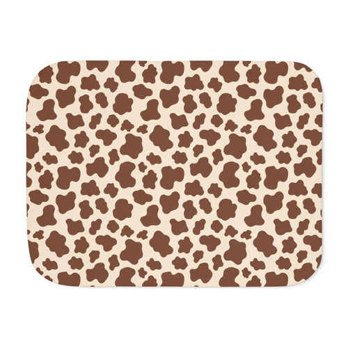 Brown cow print sherpa blanket laid flat, showing chocolate brown patches on a cream ground with a white sherpa edge