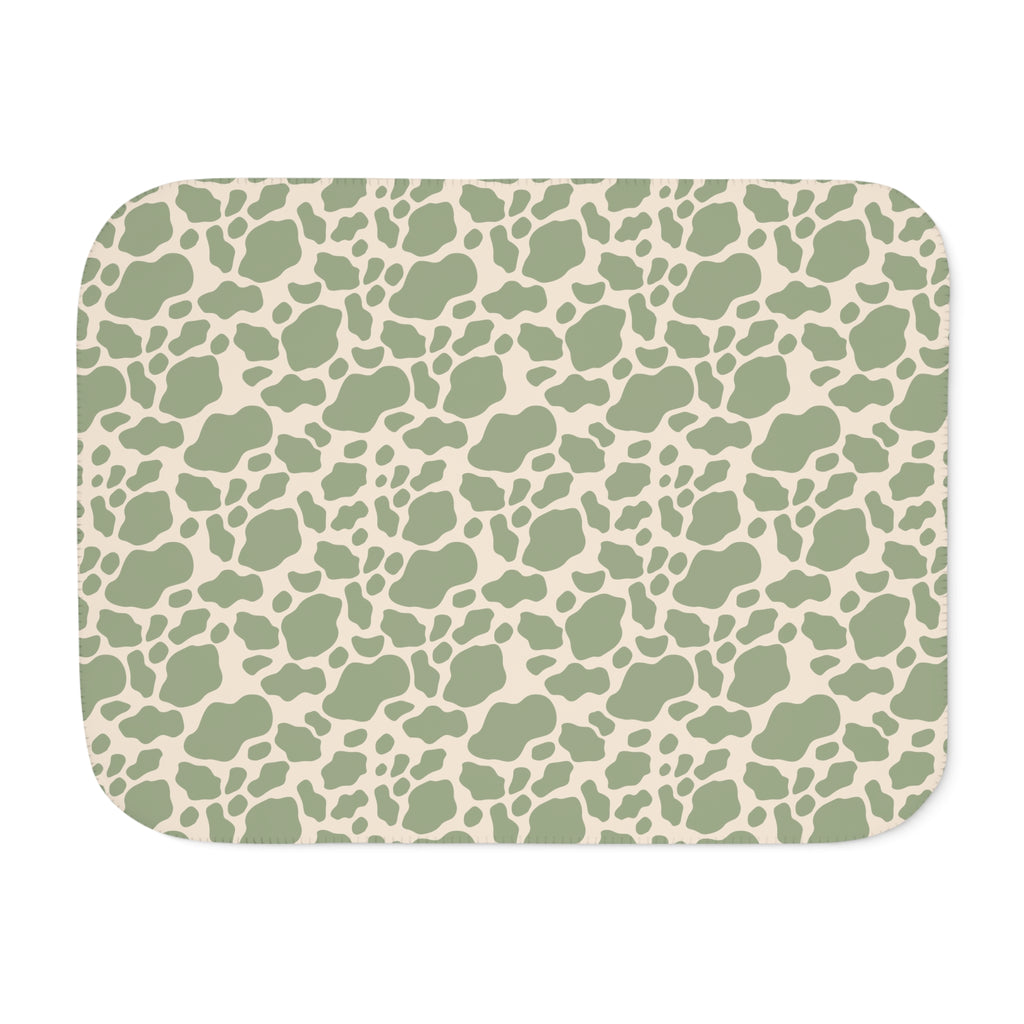 Green cow print sherpa blanket laid flat, showing sage green patches on a cream ground with a white sherpa edge