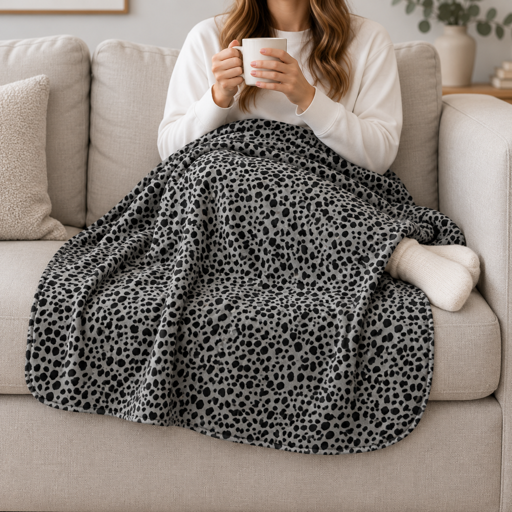 Person relaxing on a couch under the Grey Cheetah Print Sherpa Blanket
