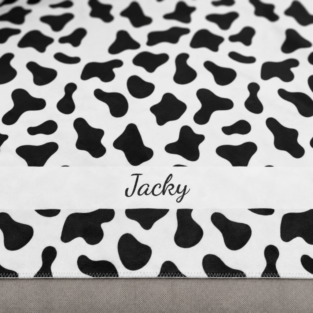 Personalized black and white cow print sherpa blanket with name, close-up of the name in script on the band