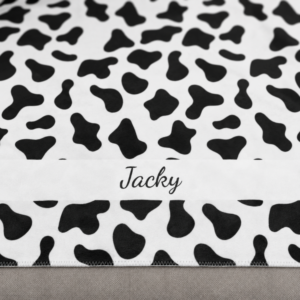 Personalized black and white cow print sherpa blanket with name, close-up of the name in script on the band