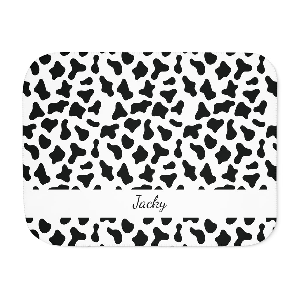 Personalized black and white cow print sherpa blanket with name, front view with name band