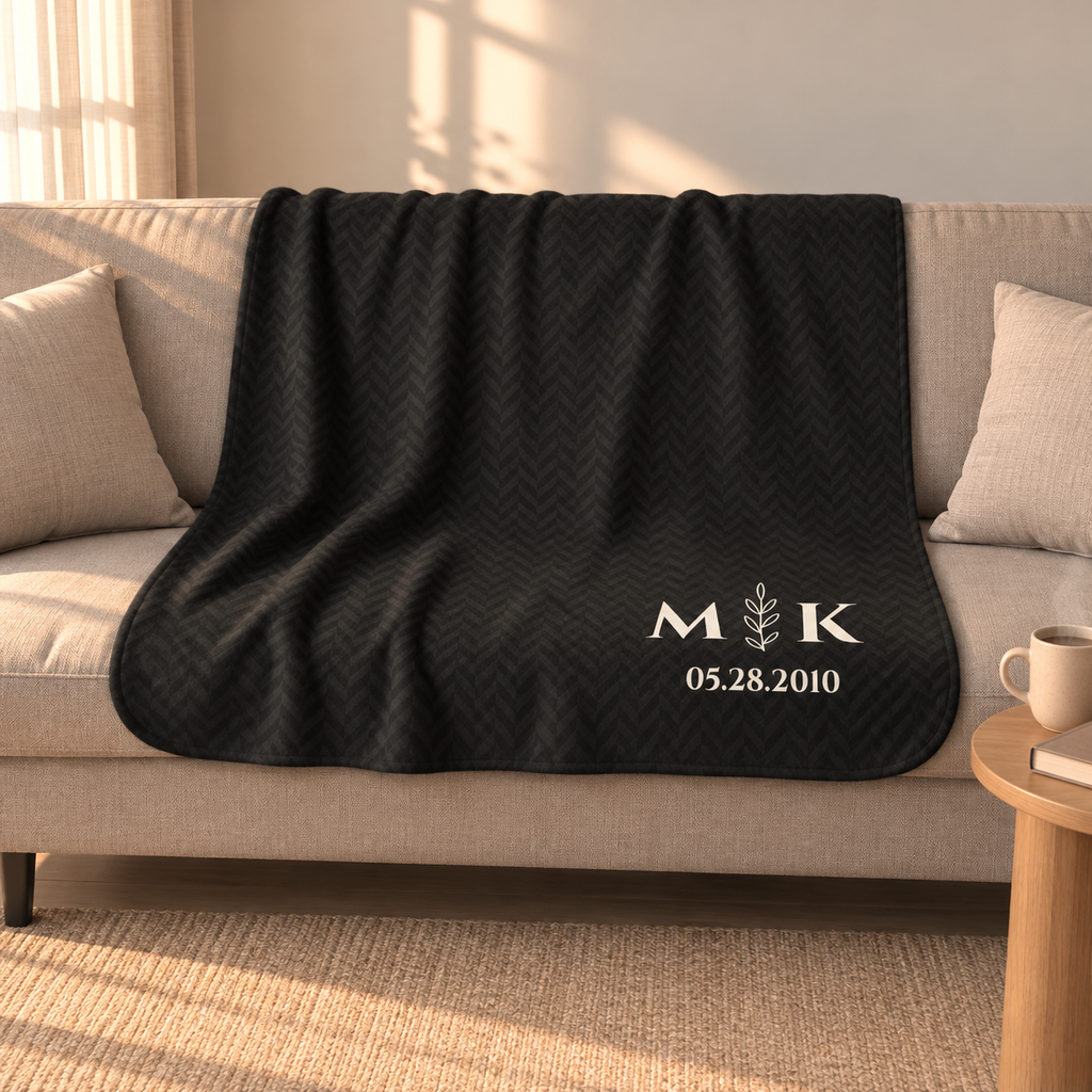 Personalized black sherpa blanket with monogram, draped over a couch