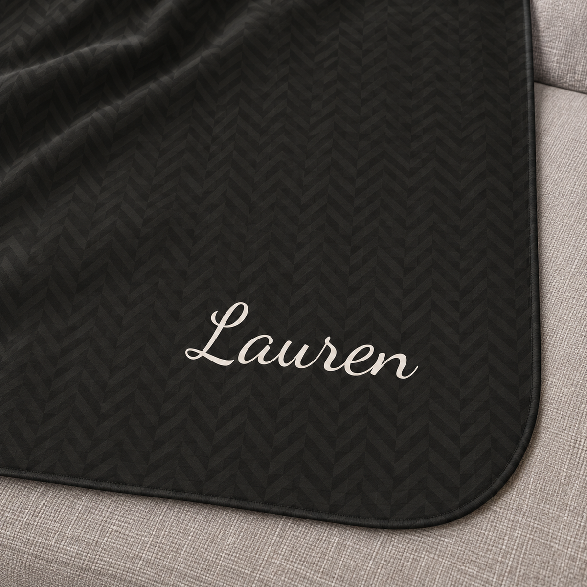 Personalized black sherpa blanket with name, close-up of the name in script on the herringbone weave