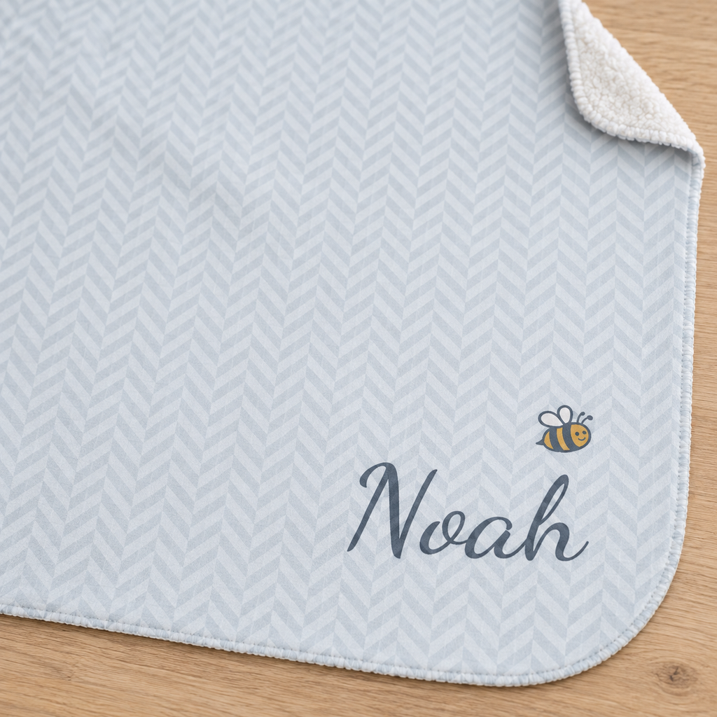 Personalized blue baby blanket with name and a bee, close-up of the name and bee on the herringbone weave