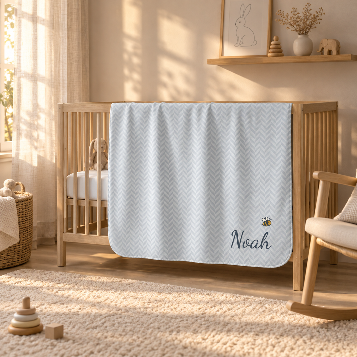 Personalized blue baby blanket with name and a bee, draped over a crib rail