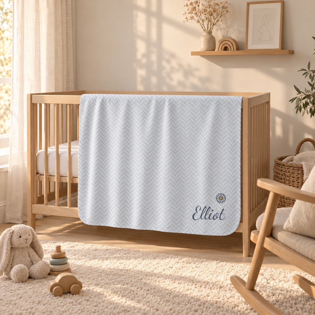 Personalized blue baby blanket with name and a flower, draped over a crib rail