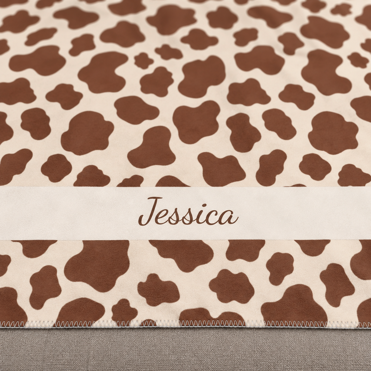 Personalized brown cow print sherpa blanket with name, close-up of the name in script on the band