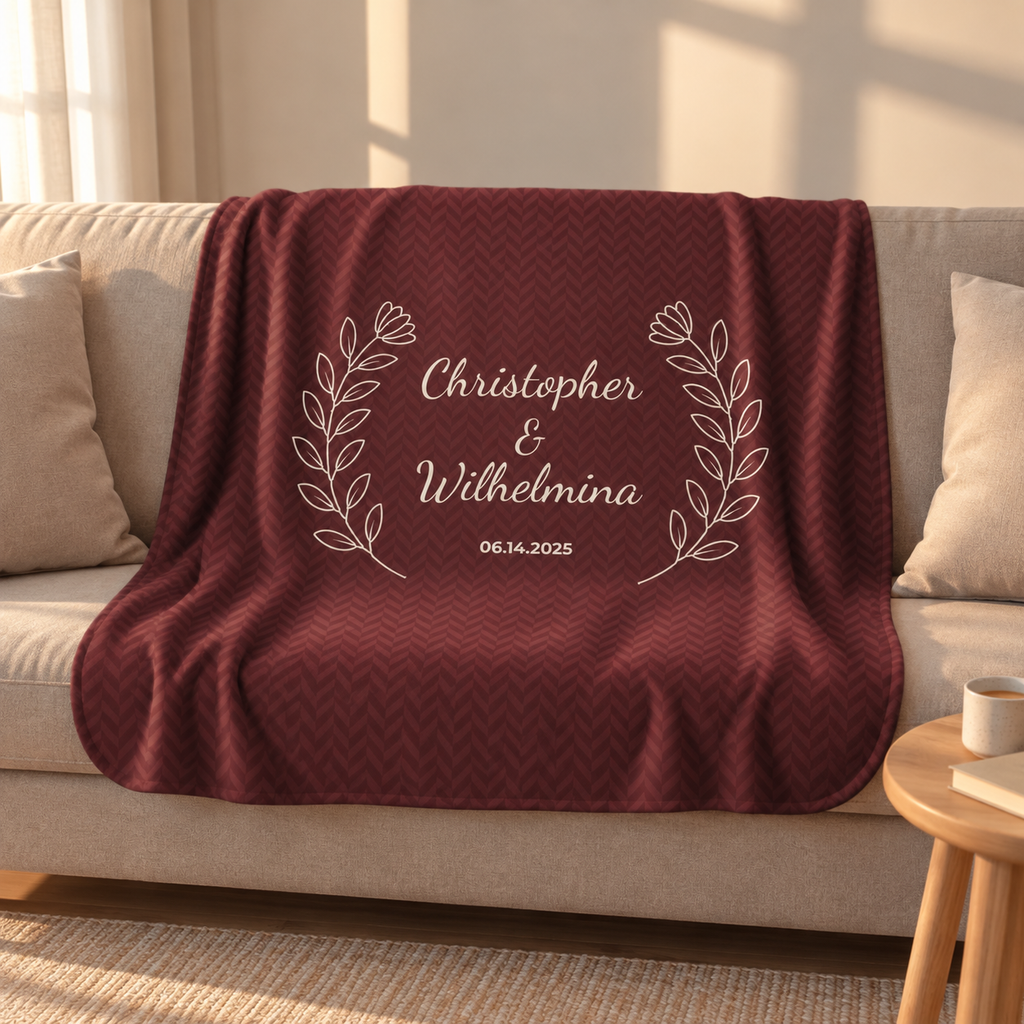 Personalized burgundy sherpa blanket with two names and a date, draped over a couch