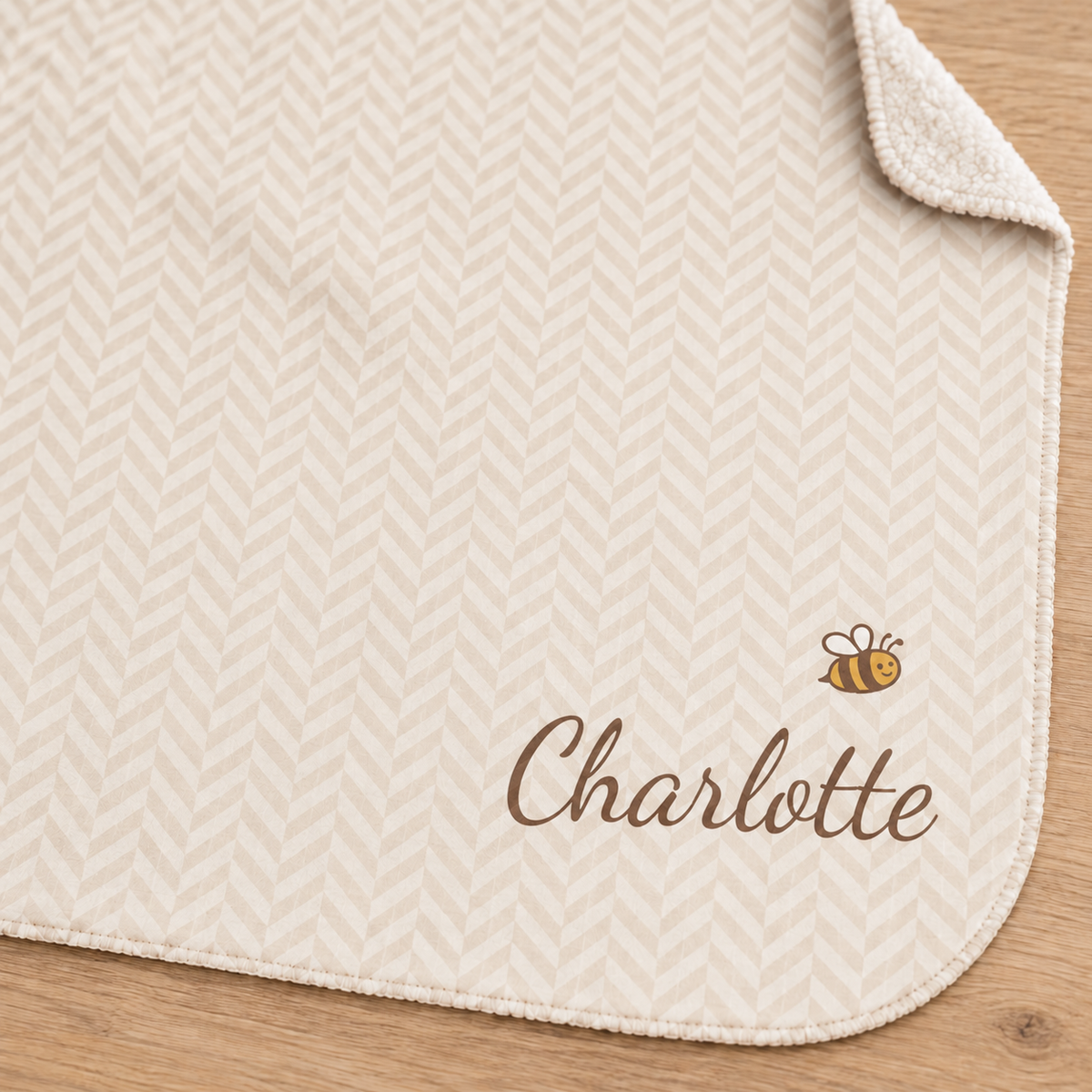 Personalized cream baby blanket with name and a bee, close-up of the name and bee on the herringbone weave