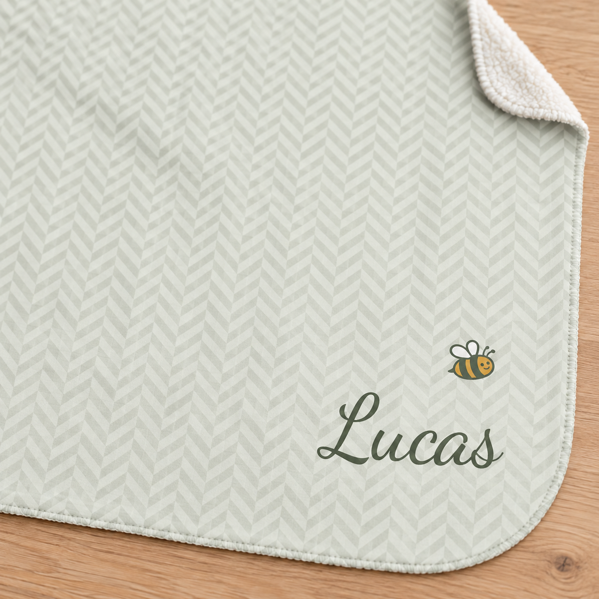 Personalized green baby blanket with name and a bee, close-up of the name and bee on the herringbone weave