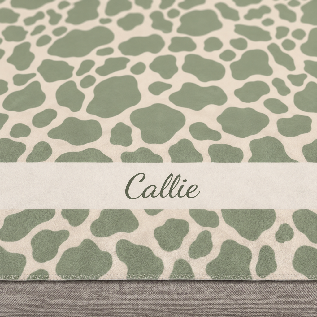 Personalized green cow print sherpa blanket with name, close-up of the name in script on the band