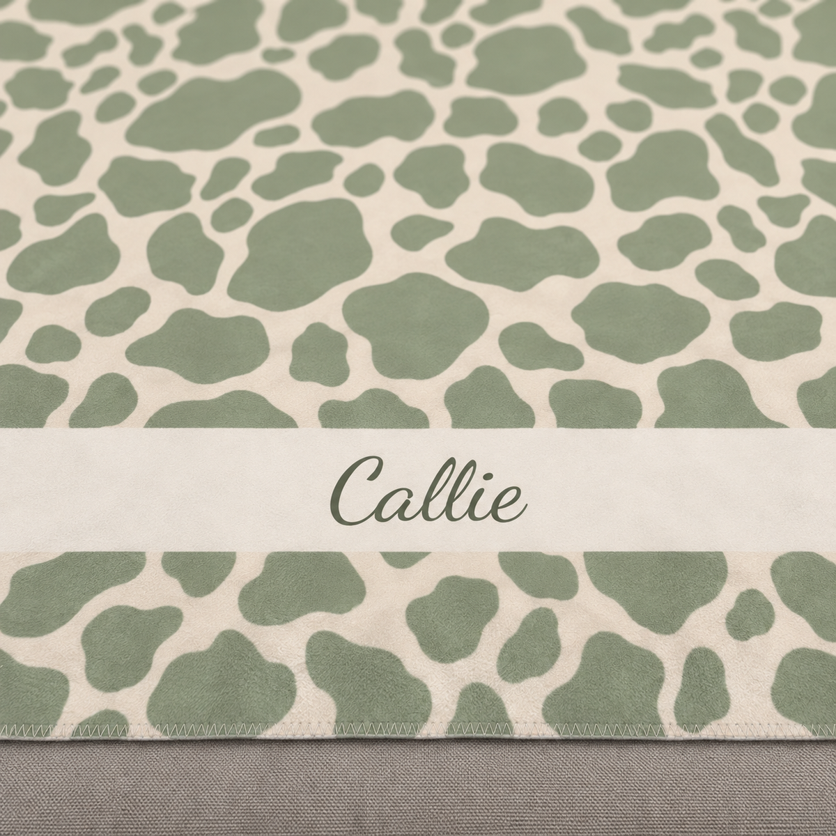 Personalized green cow print sherpa blanket with name, close-up of the name in script on the band